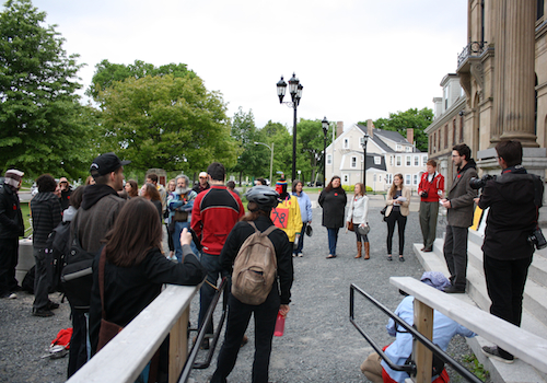 Pamela Ross asks the crowd to go to the front of the N.B. Legislature lawn so that Charles LeBlanc, the blogger banned from the Legislature grounds, can document the rally in support of students. Photo: Luc Walhain. adam-2