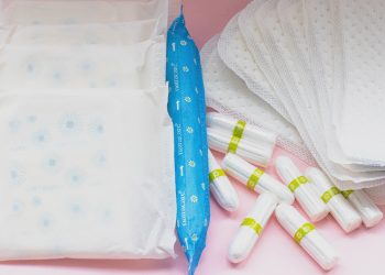 Cotton period products, including tampons, applicator tampons, pads, curved panty liners, are pictured against a pink background.