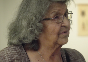 A woman with grey-black hair and glasses is pictured in profile.