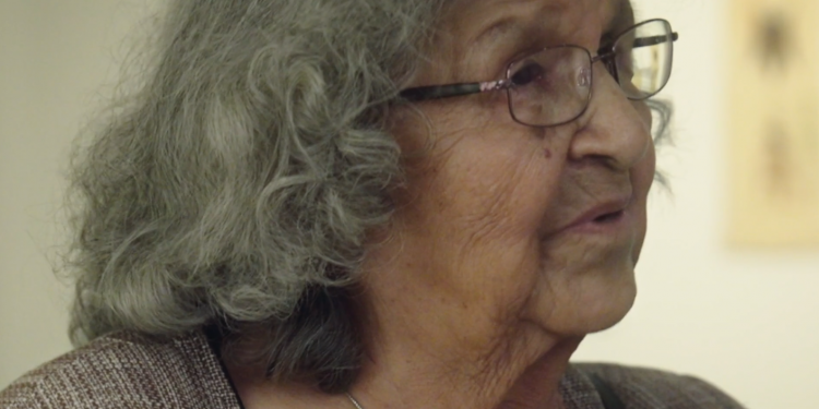 A woman with grey-black hair and glasses is pictured in profile.