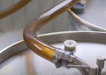 Amber-brown maple syrup runs through a clear tube connected to metal equipment.