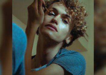 A person applies makeup in dramatic lighting.