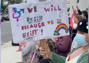 A protester holds a sign that says, "We will resist because we exist!"