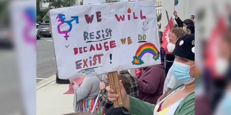 A protester holds a sign that says, "We will resist because we exist!"