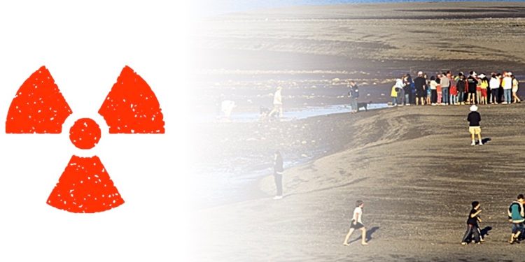 A group of people are gathered on a dirt mound. A red radioactive symbol is next to them.