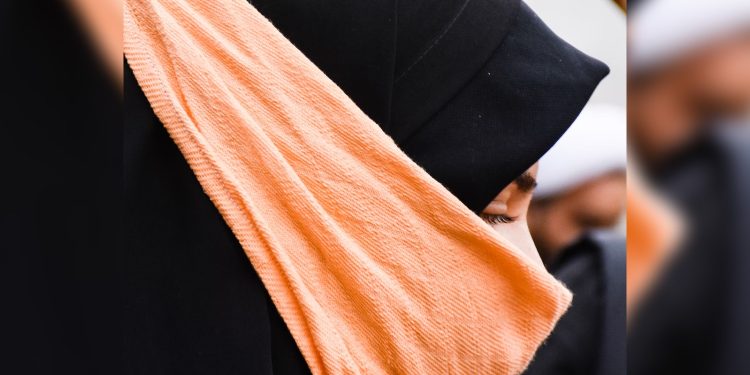 A woman wearing a black head covering and an orange bandana.
