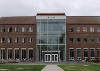 An imposing brick building about four storeys high with what appears to be a central glass atrium and the name Irving written on the facade is pictured on a college campus.